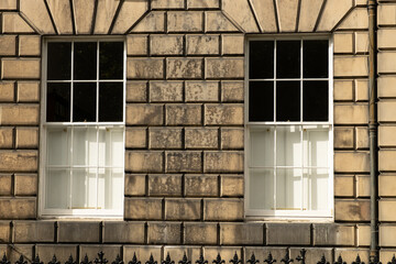 Two identical traditional white sash windows in stone wall of house in Edinburgh, Scotland