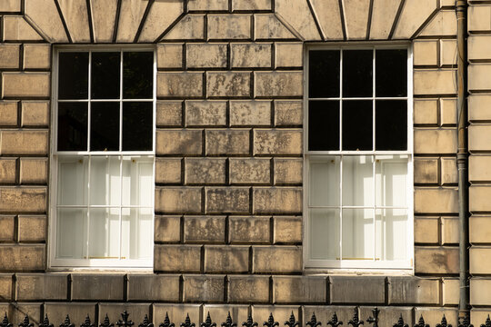 Two identical traditional white sash windows in stone wall of house in Edinburgh, Scotland