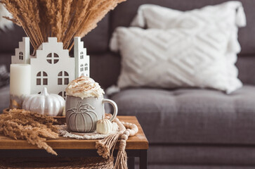 Fototapeta na wymiar A seasonal drink. Delicious pumpkin latte with whipped cream and cinnamon in a mug on a wooden table in the living room interior.Autumn decor in the house. Scandinavian style.