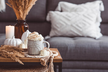 Fototapeta na wymiar A seasonal drink. Delicious pumpkin latte with whipped cream and cinnamon in a mug on a wooden table in the living room interior.Autumn decor in the house. Scandinavian style.