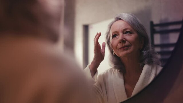 Happy woman in her 60s pleased with mirror reflection, beauty routine, skincare