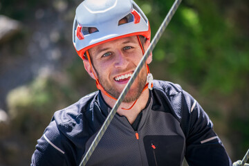 A man in a helmet and black jacket smiles while rock climbing.