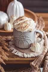 Obraz na płótnie Canvas A seasonal drink. Delicious pumpkin latte with whipped cream and cinnamon in a mug on a wooden table in the living room interior.Autumn decor in the house. Scandinavian style.