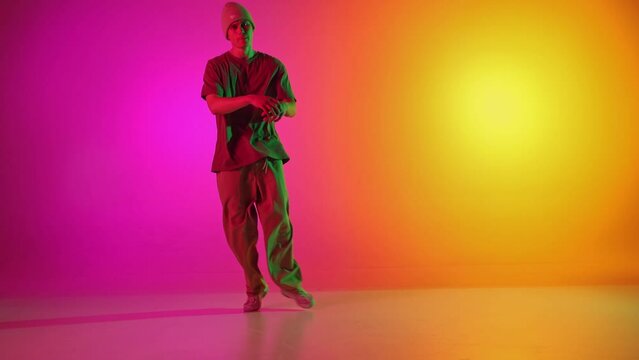 Cool attitude young man, talented freestyle dancer dancing in motion in neon light against gradient pink-yellow background. Concept of hobby, sport, creativity, fashion and style, motion, action. Ad
