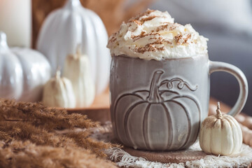 A seasonal drink. Delicious pumpkin latte with whipped cream and cinnamon in a mug on a wooden table in the living room interior.Autumn decor in the house. Scandinavian style.