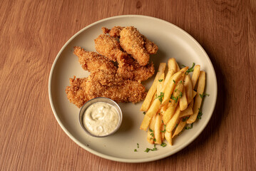 Tiras de pollo frito con mayonesa y papas fritas, en fondo de madera en un plato blanco