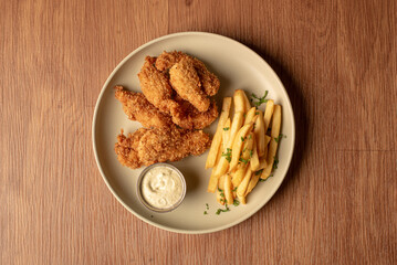 Tiras de pollo frito con mayonesa y papas fritas, en fondo de madera en un plato blanco