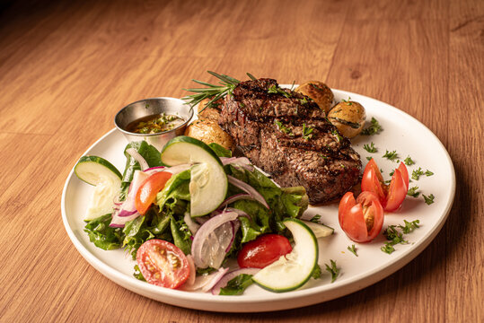 Fotograf&iacute;a corte de carne a la parilla acompa&ntilde;adas de papas fritas y salteadas, con una ensalada verde y aderezo