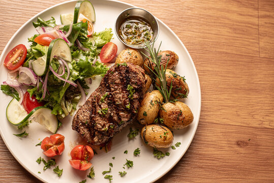 Fotograf&iacute;a corte de carne a la parilla acompa&ntilde;adas de papas fritas y salteadas, con una ensalada verde y aderezo