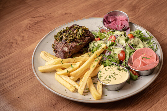 Fotograf&iacute;a corte de carne a la parilla acompa&ntilde;adas de papas fritas y salteadas, con una ensalada verde y aderezo