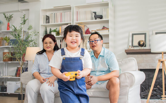 Asian little girl playing with family camera toy with concentration, taking photo shot with fun, standing in cozy living room at home. Education, Kid, Activity, Interior house Concept.
