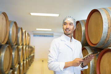 Winemaker inspecting quality tank of fermentation during manufacturing in winery factory. Male...