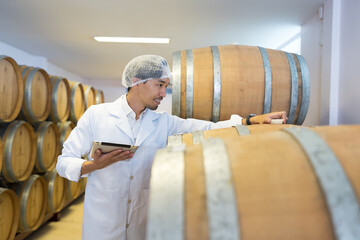Winemaker inspecting quality tank of fermentation during manufacturing in winery factory. Male...