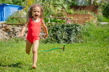 Screaming girl in red swimsuit running through sprinkler water