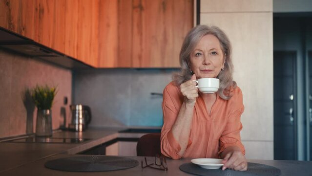 Attractive senior woman drinking coffee in the kitchen, morning ritual, rest