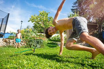 Teenager does handstand on a sunny, sprinkler-watered garden