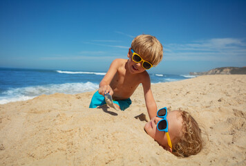 On the beach, two kids in sunglasses enjoy playtime with sand