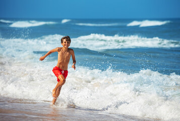 A young boy runs joyfully along the shoreline with ocean waves
