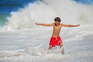 Boy, in red swim shorts with outstretched arms have fun at waves