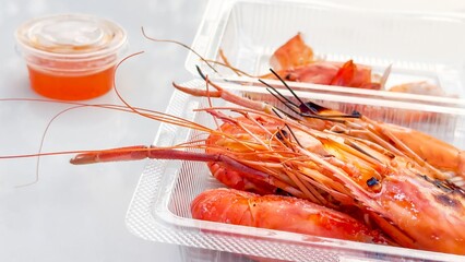 Street food. Plump, grilled prawns in a transparent takeaway box, paired with a tangy dipping...