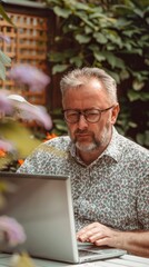 Portrait of modern middle-aged man with pleasant appearance working with laptop in home garden, home office, online work, calm and focused