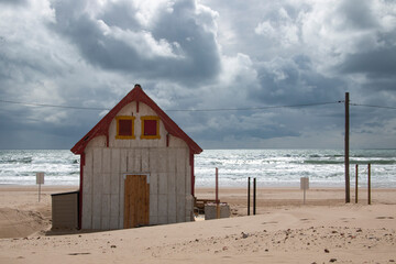 Abandoned wooden house on a beach with the sea in the background and a cloudy blue sky