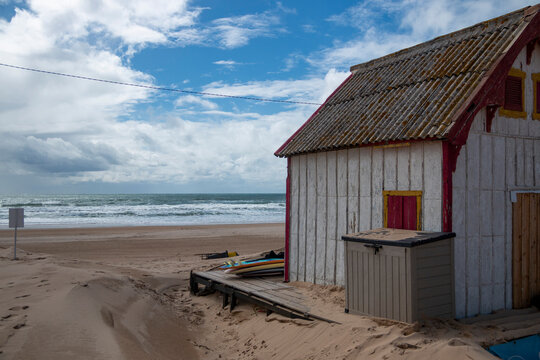 Abandoned wooden house on a beach with the sea in the background and a cloudy blue sky