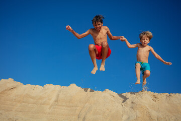 Pair of cheerful children jump from a sandbank against blue sky