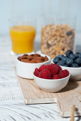 fresh berries, nuts, muesli and orange juice on white table, vertical