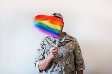 A handsome man in camouflage military uniform and a multicolored pride flag.