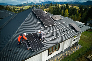Technicians building photovoltaic solar module station on roof of house. Men roofers in helmets...