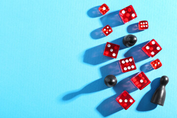 Many red dices and color game pieces on light blue background, flat lay. Space for text