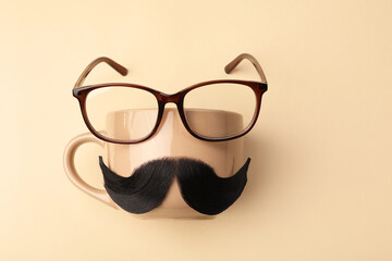 Artificial moustache, cup and glasses on beige background, top view. Space for text