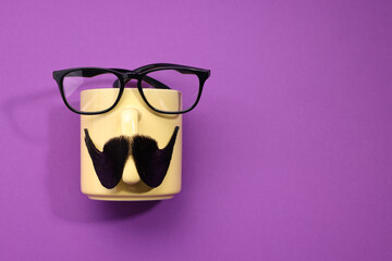 Man's face made of artificial mustache, cup and glasses on purple background, top view. Space for...