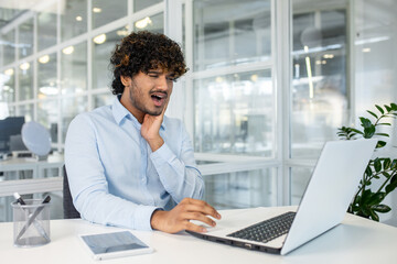 An Indian professional experiences discomfort from a toothache while working on his laptop in a bright office environment. The pain disrupts his work routine. - obrazy, fototapety, plakaty