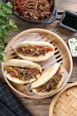 Delicious gua bao in bamboo steamer on wooden table, flat lay