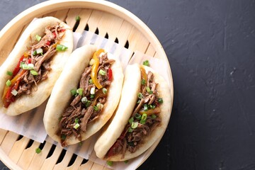 Delicious gua bao in bamboo steamer on black table, top view. Space for text
