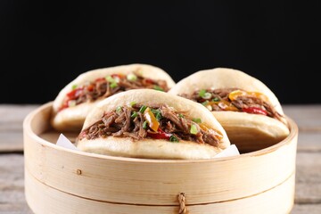 Delicious gua bao in bamboo steamer on wooden table, closeup - obrazy, fototapety, plakaty