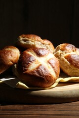 Tasty hot cross buns on wooden table against dark background, closeup