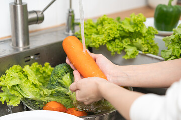 Close up asian young woman washing carrot, tomato, broccoli  fresh vegetables, paprika with splash water in basin of water on sink in kitchen, preparing fresh salad, cooking meal. Healthy food people.