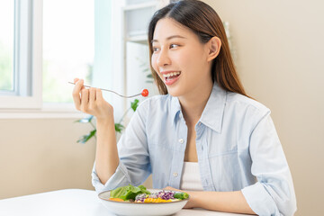 Diet concept, happy asian young woman hand use a fork to prick tomato, fresh vegetable or green salad, eat nutrition food  on table at home, low fat to good body. Girl getting weight loss for healthy. - obrazy, fototapety, plakaty