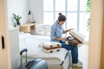 Young woman packing suitcase in the bedroom, preparing for travel
