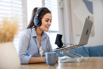 Woman wearing headphones sitting at a desk speaking into microphone and recording a podcast

