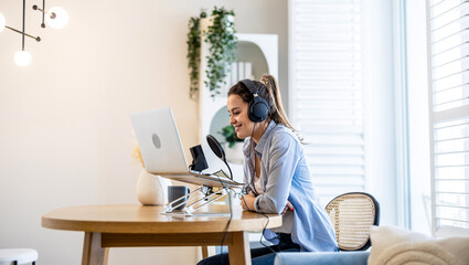 Woman wearing headphones sitting at a desk speaking into microphone and recording a podcast
