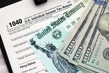 United States 1040 tax form individual income tax return with refund check and US dollar bills...