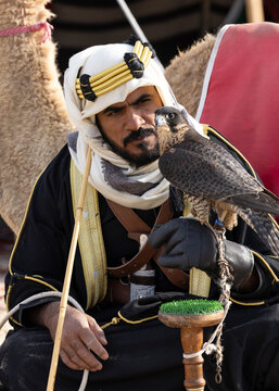 Saudi man in traditional clothing with his camel in a desert