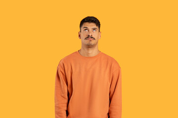 Millennial guy looking up, puzzled against yellow background
