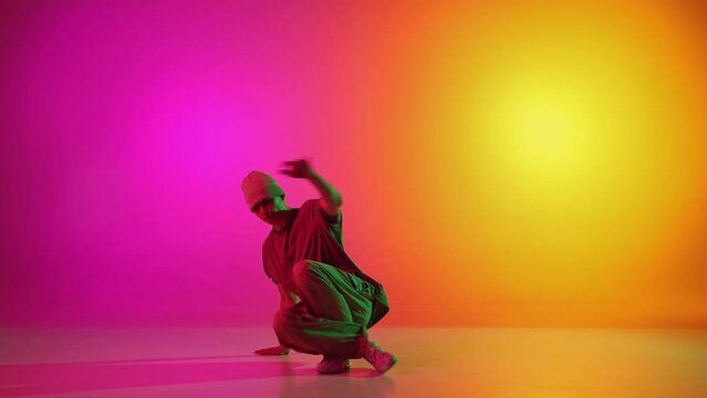 Artistic, young man, break-dancer dancing in motion in neon light against gradient pink-yellow background. Concept of hobby, sport, creativity, fashion and style, motion, action. Ad
