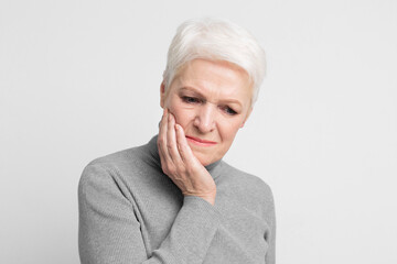Elderly woman holding cheek in pain on grey background