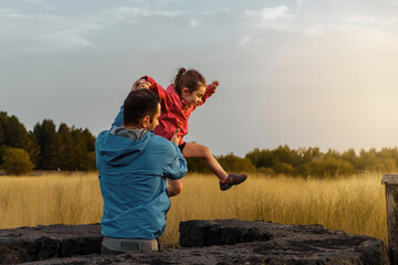 Family fun outdoor - child leaps from a stone wall into father's arms against the glowing backdrop...